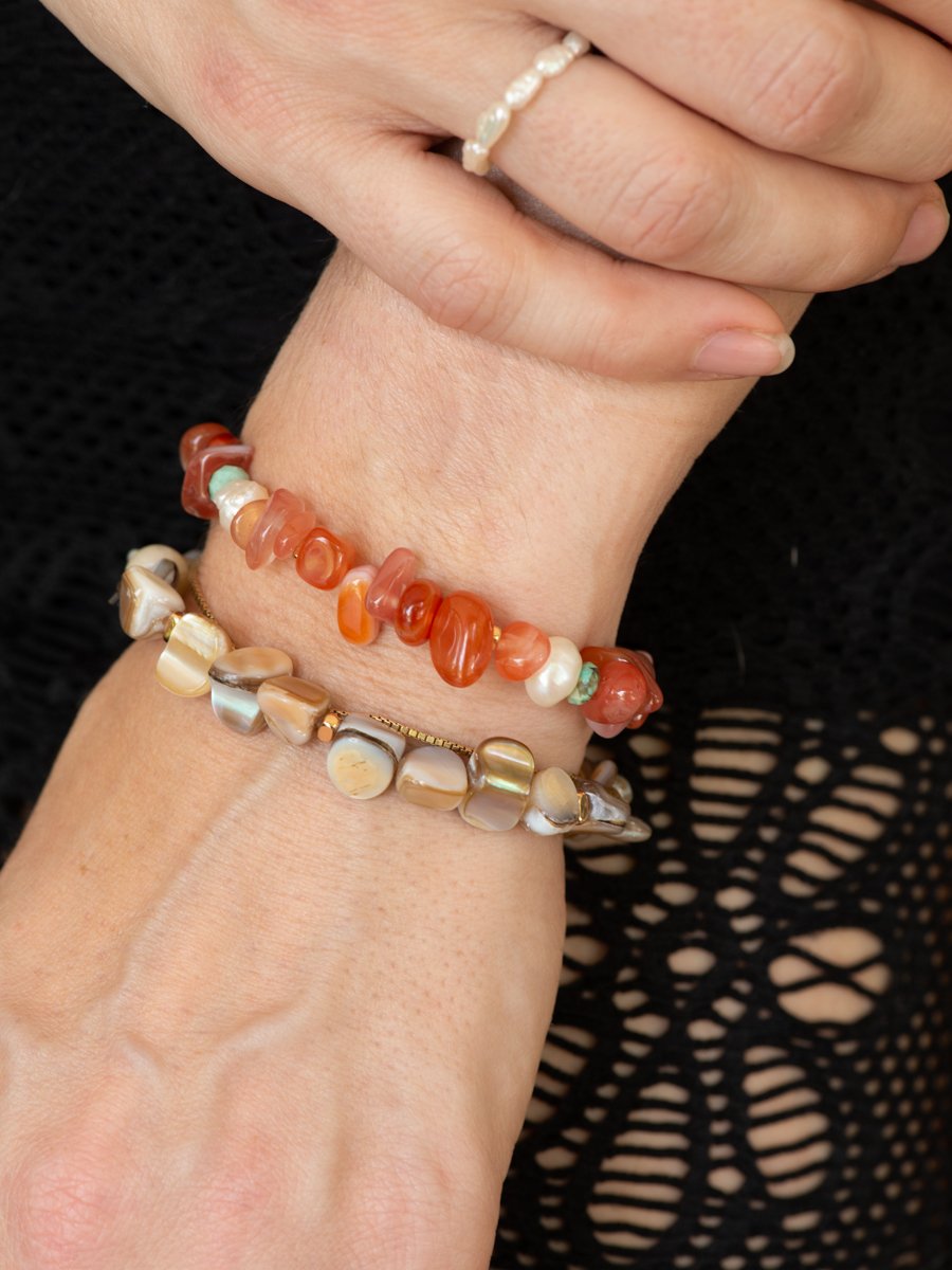 Close-up of a hand wearing two beaded bracelets on a black background