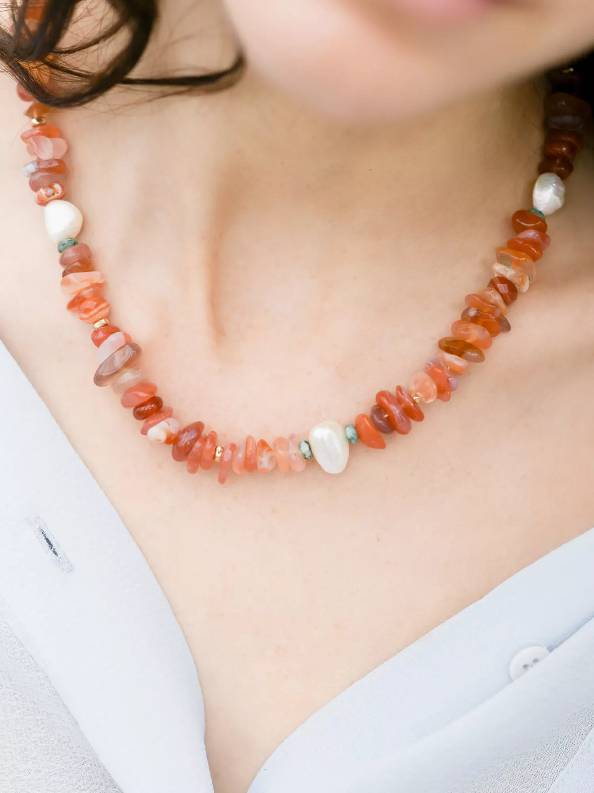 Necklace with orange beads and pearls on a person wearing a light blue shirt.
