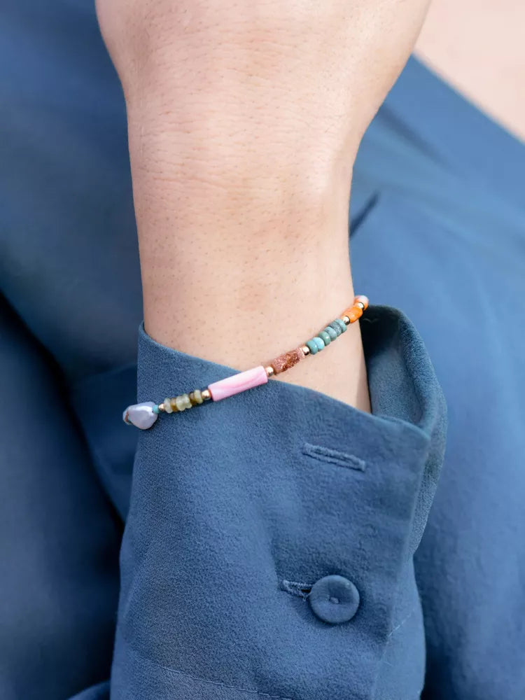 Close-up of a wrist wearing a colorful beaded bracelet against a blue background.