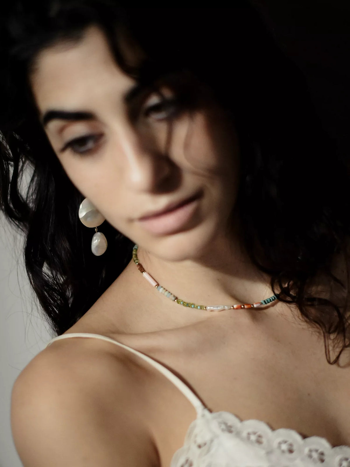 Close-up of a woman wearing a necklace and drop earrings with a dark background
