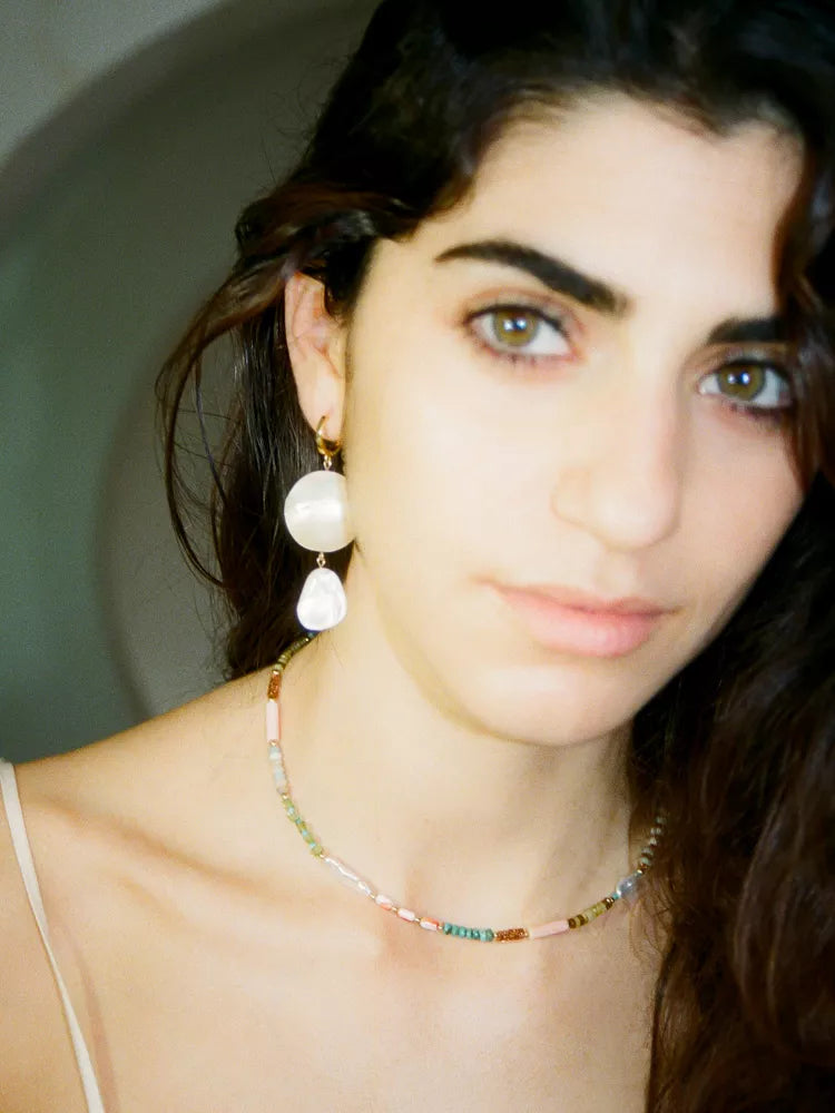 Close-up of a woman wearing earrings and a necklace with a neutral background