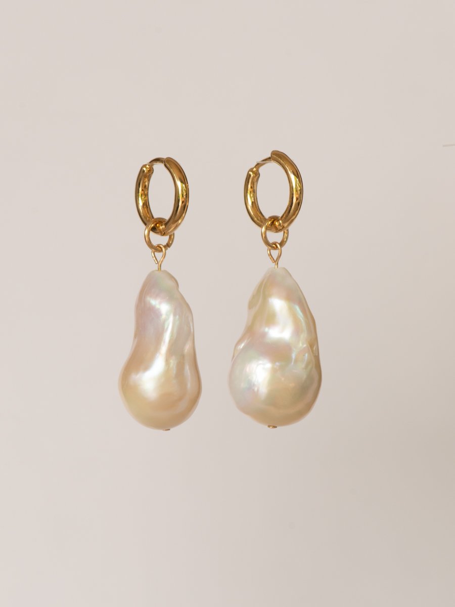 Pair of gold hoop earrings with large pearl drops on a beige background