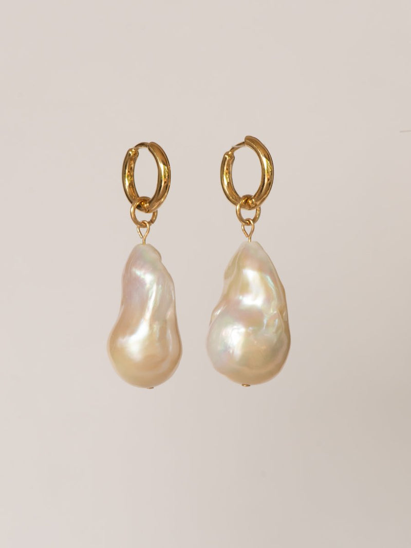 Pair of gold hoop earrings with large pearl drops on a beige background