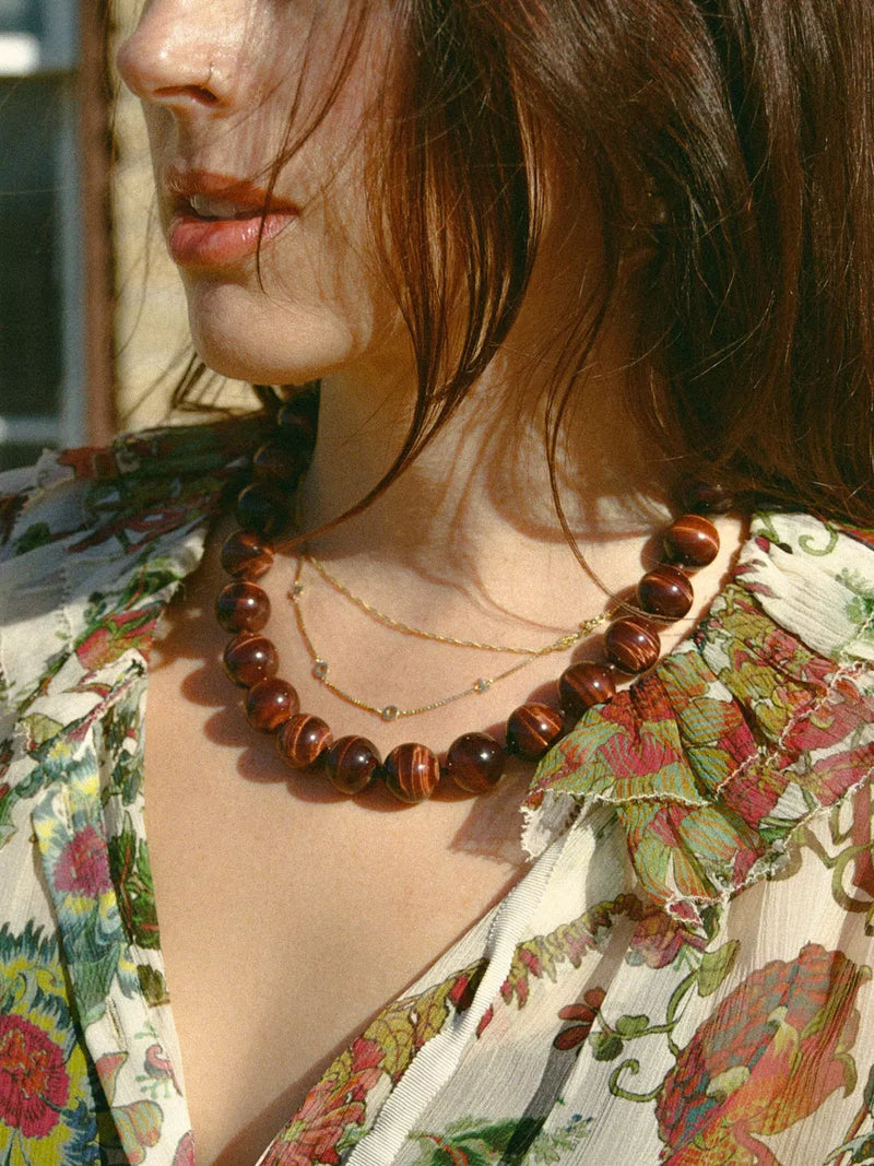 Close-up of a person wearing a floral dress and a necklace with tigers eye beads.