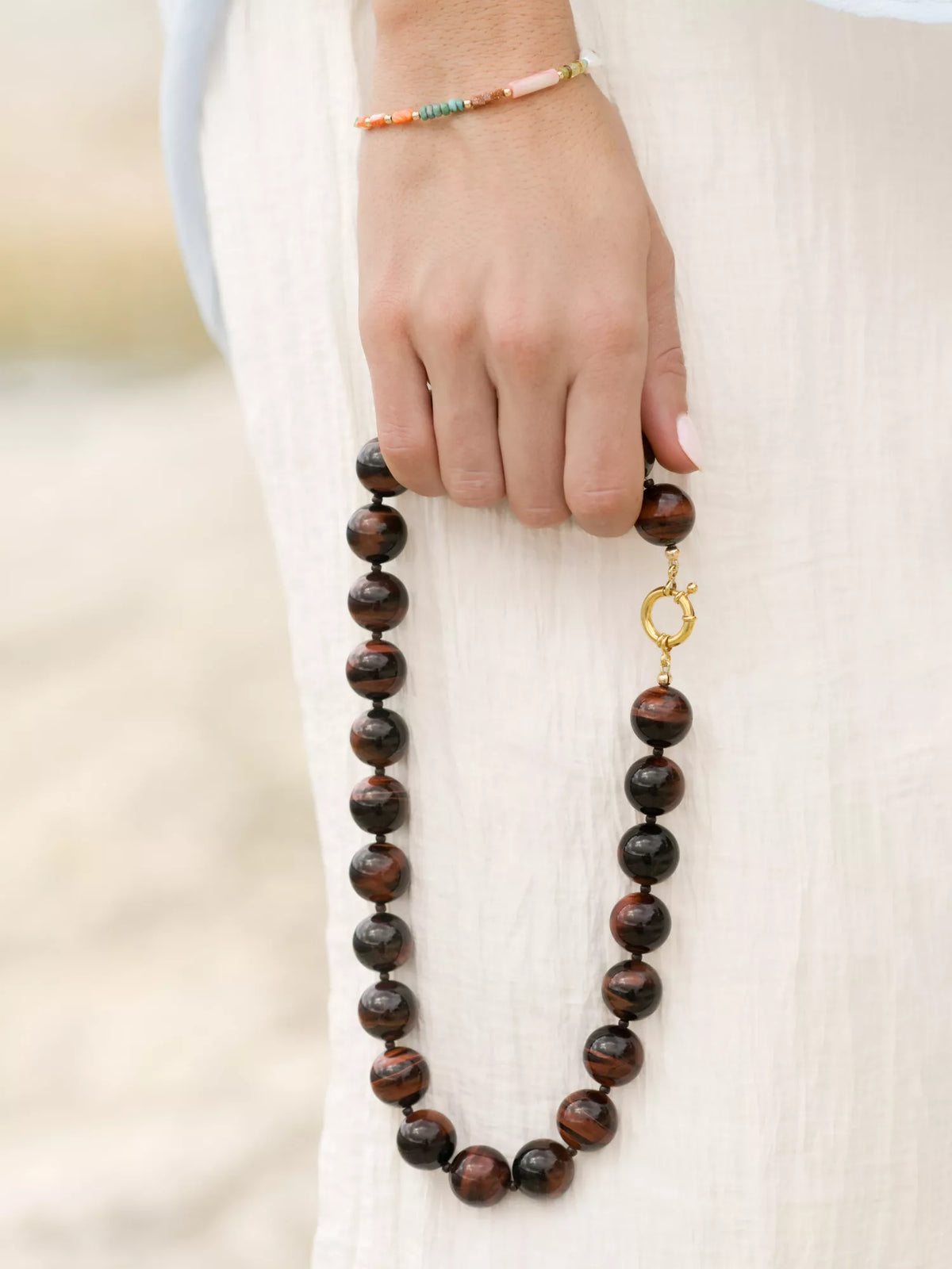 Hand holding a tiger's eye beaded necklace with a gold clasp against a neutral background