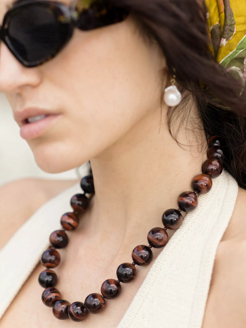 Close-up of a woman wearing a tigers eye beaded necklace and sunglasses.