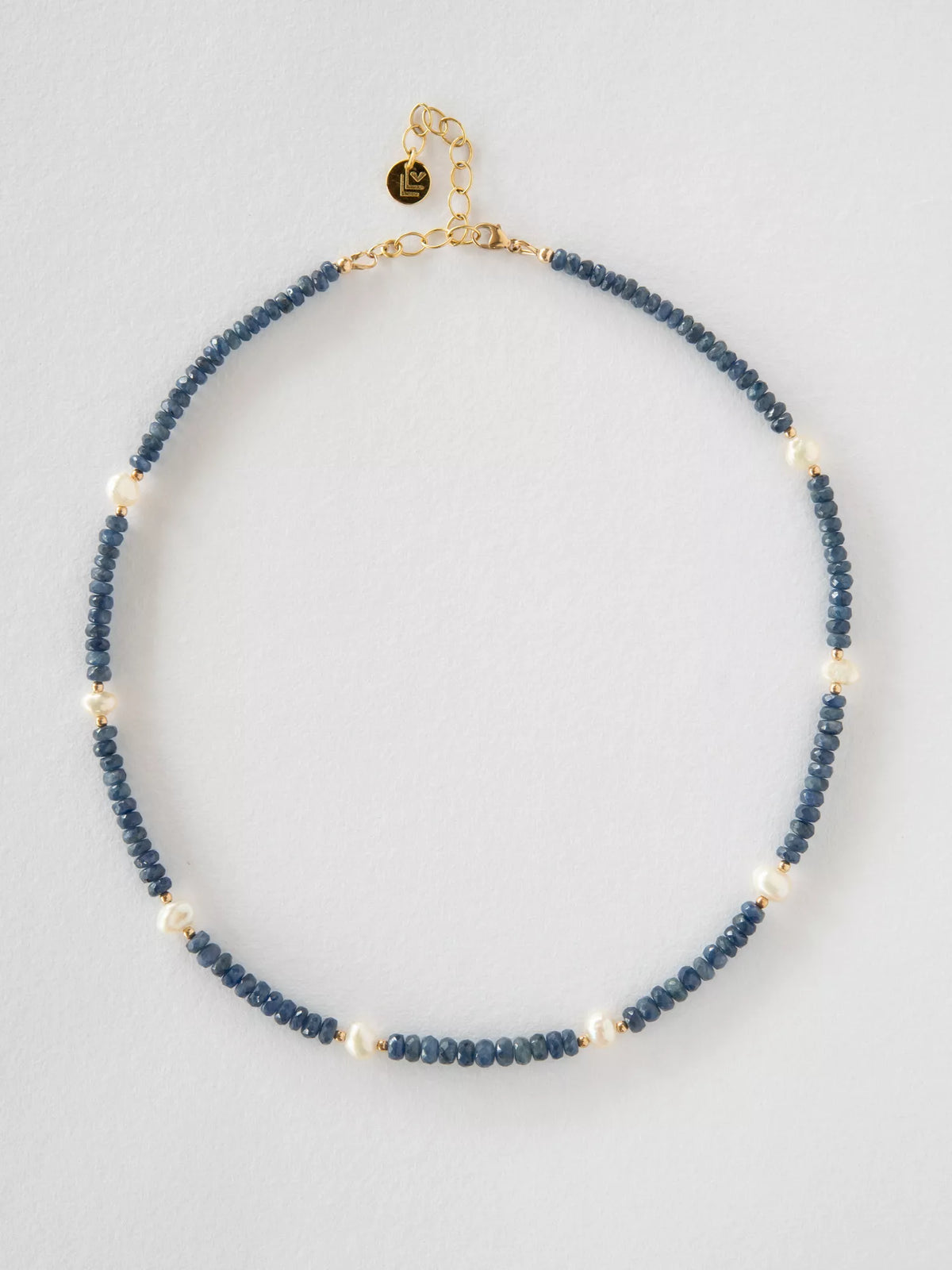Necklace with blue sapphire beads and gold clasp on a light gray background