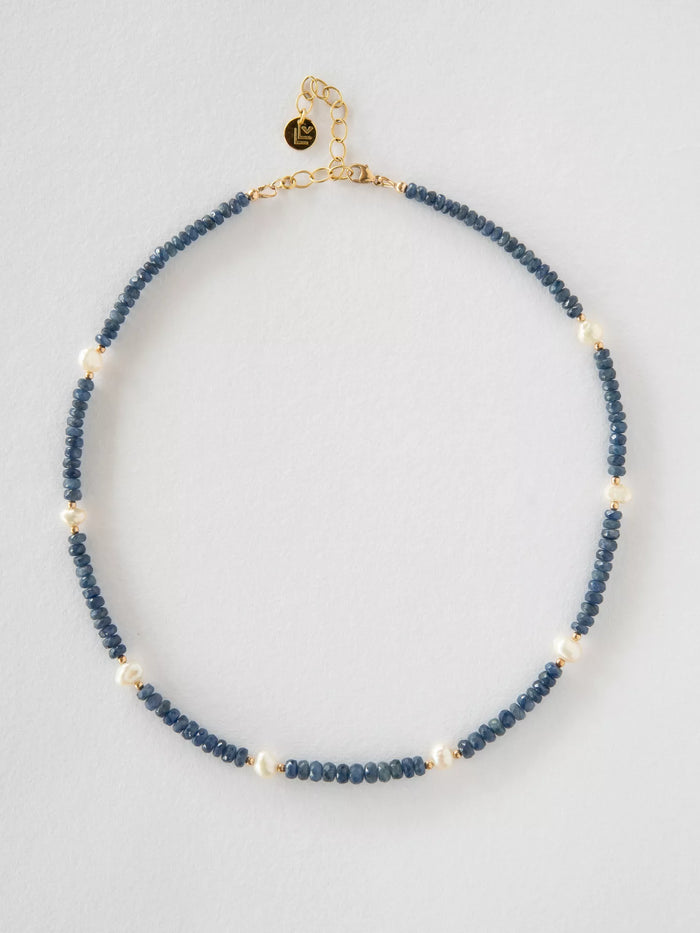 Necklace with blue sapphire beads and gold clasp on a light gray background
