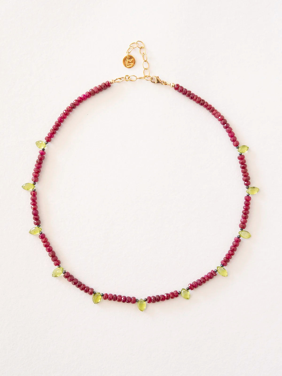 A beaded necklace featuring deep red ruby beads with peridot accents and gold chain and clasp, displayed on a clean white background.
