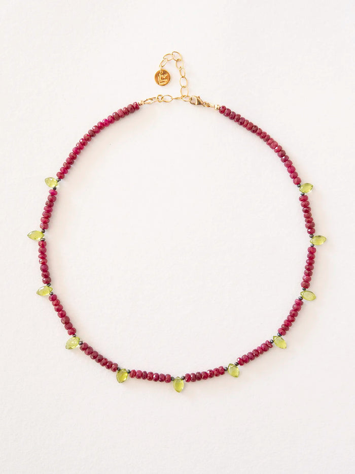 A beaded necklace featuring deep red ruby beads with peridot accents and gold chain and clasp, displayed on a clean white background.