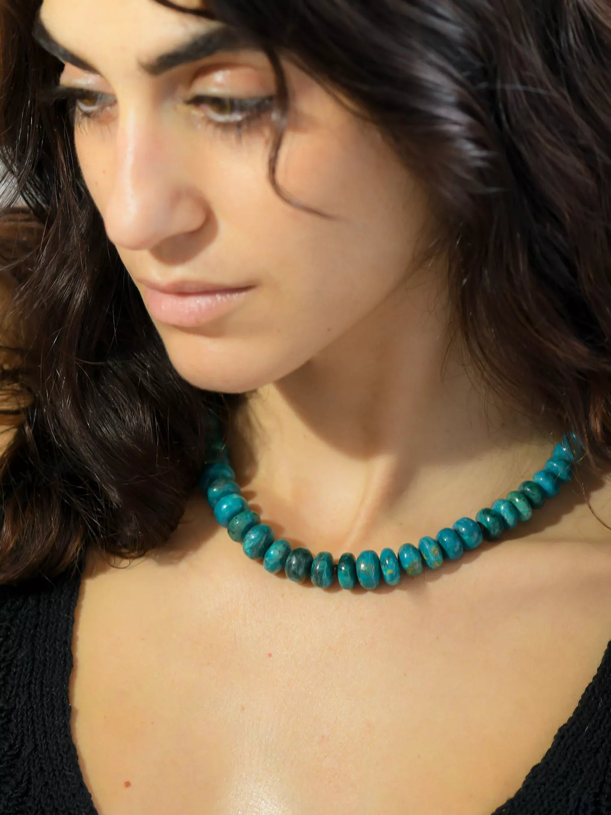 Woman wearing a teal beaded necklace with a blurred background