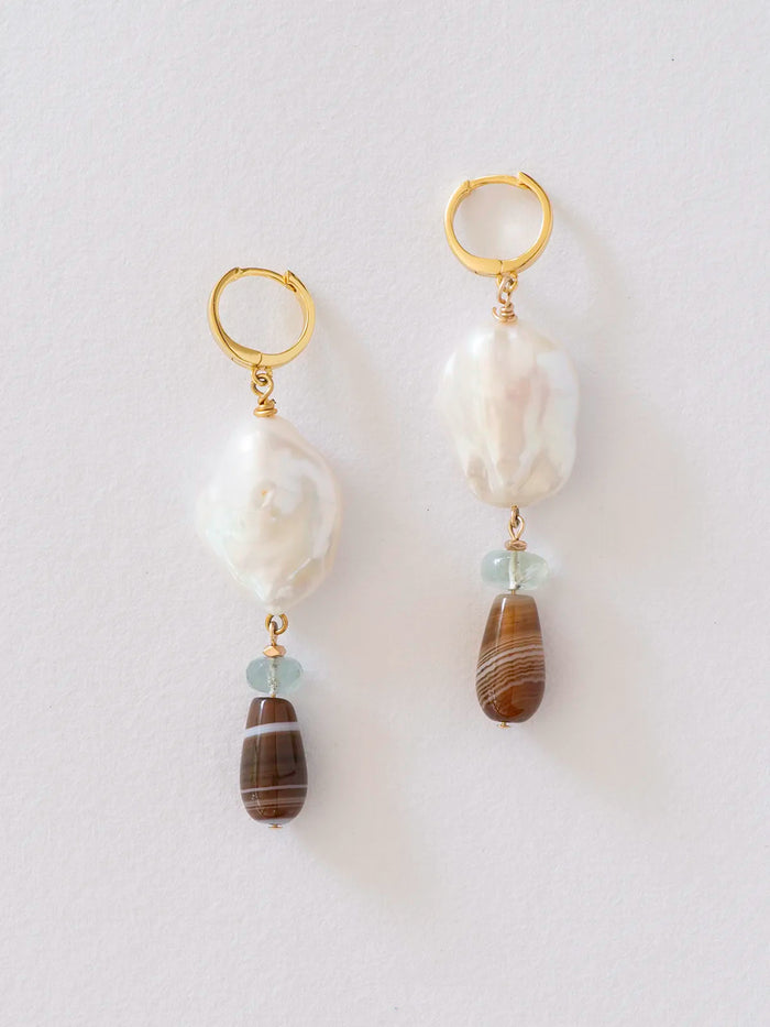 A pair of gold hoop drop earrings featuring a large white baroque pearl, a small light blue bead, and a brown striped agate bead, displayed against a clean white background.
