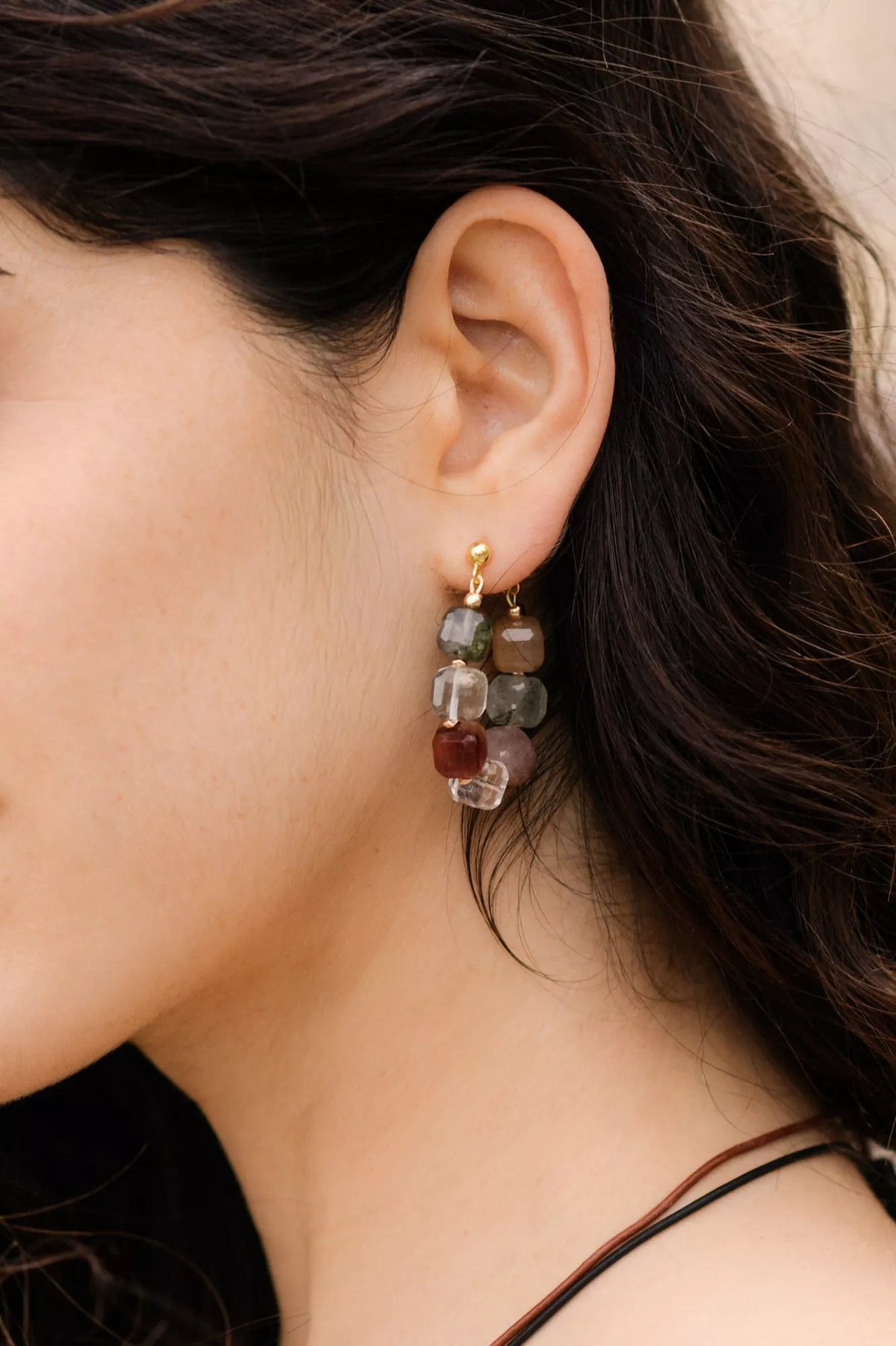 Close-up of an ear wearing a colorful gemstone earring with a blurred background