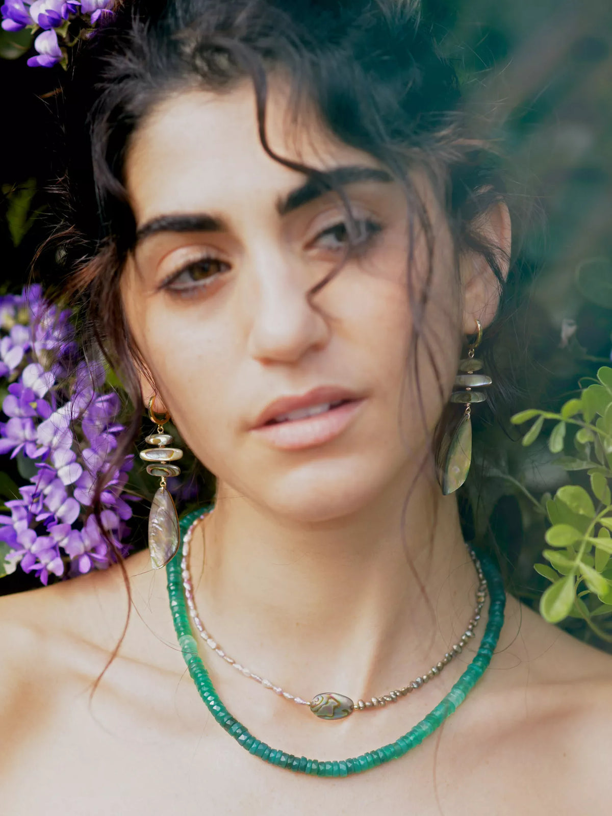 Woman wearing jewelry with a blurred background of flowers and greenery