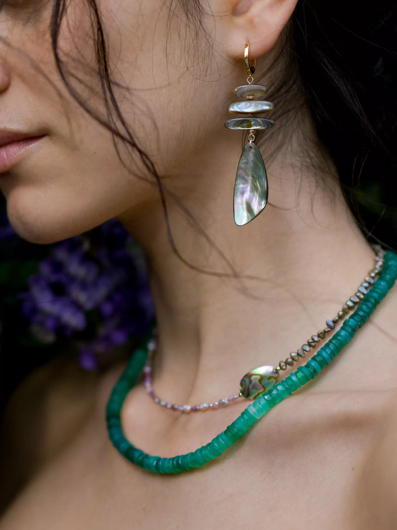 Close-up of a woman wearing a green beaded necklace and abalone earrings.