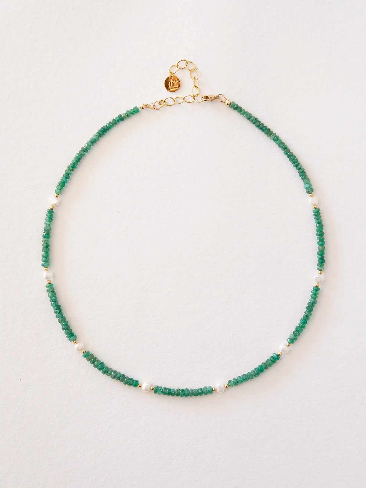 An emerald beaded necklace accented with pearls and solid gold spacer beads, finished with a gold clasp and extender chain, displayed on a clean white background.