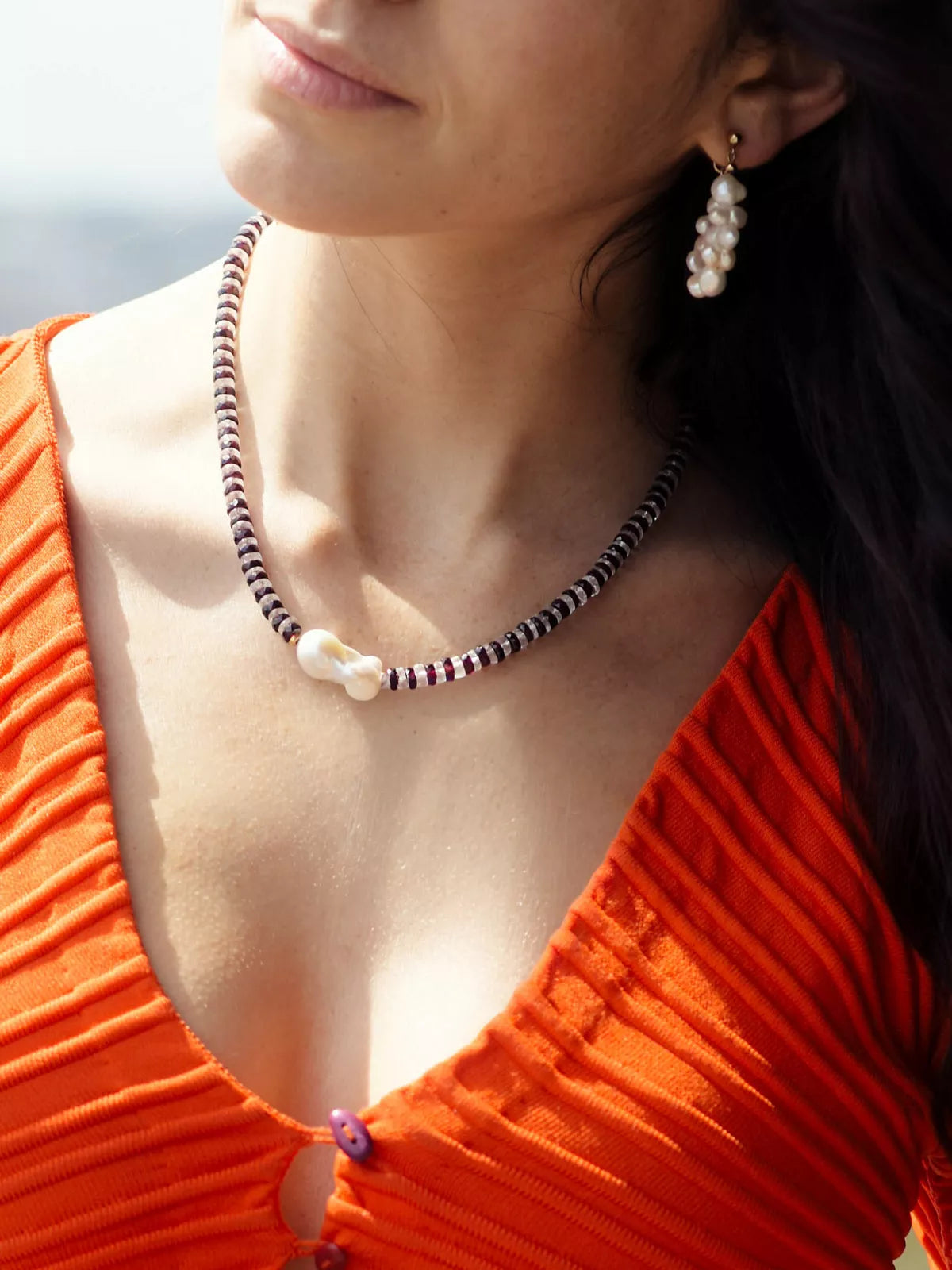 Close-up of a woman wearing a necklace and pearl earrings with a blurred background
