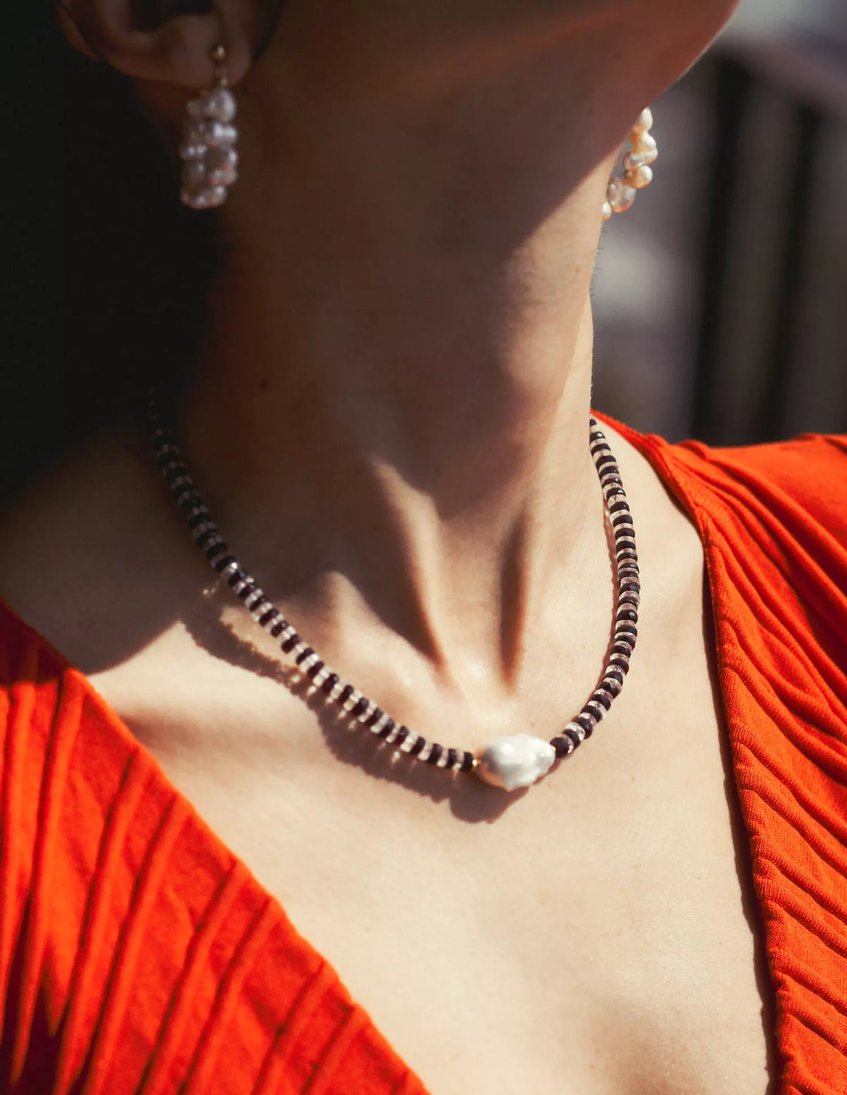 Close-up of a person wearing a necklace and earrings with a blurred background