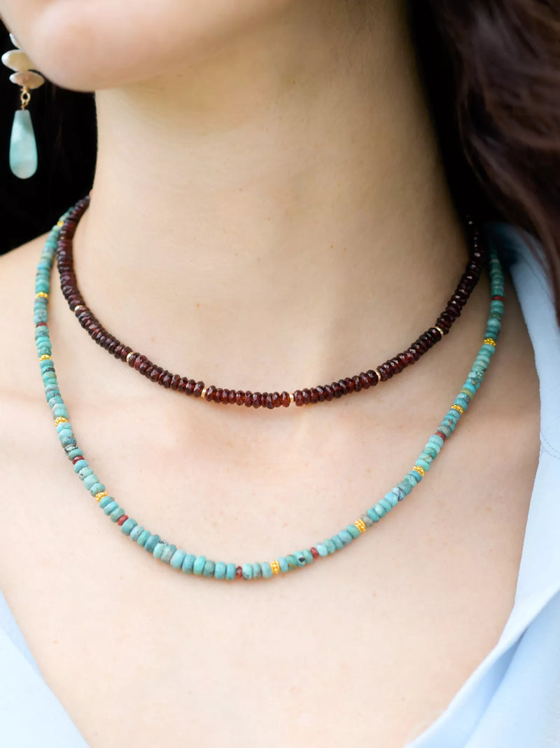 Close-up of a person wearing two beaded necklaces with a blurred background