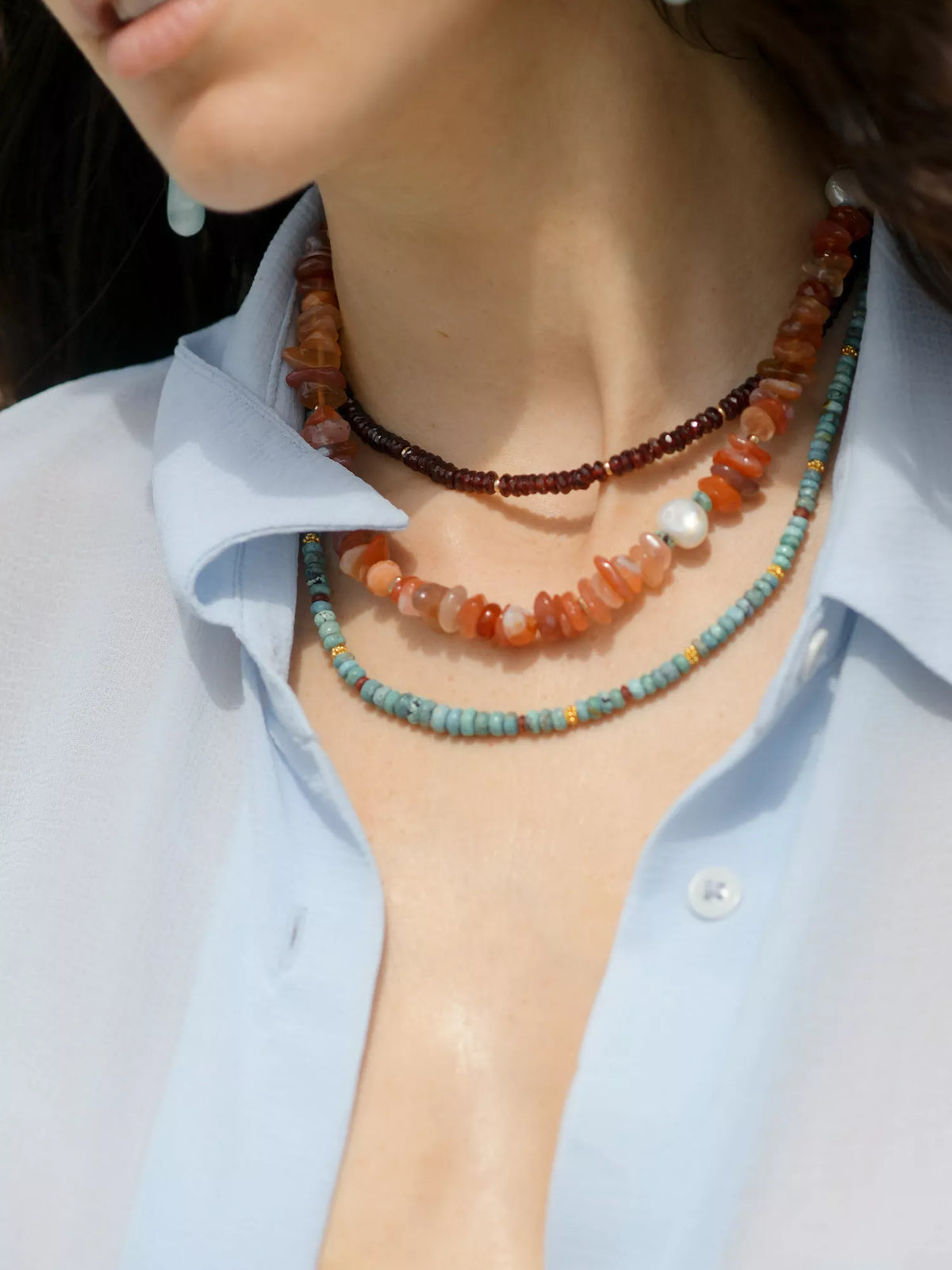 Necklace with beads and pearls worn by a person against a light background