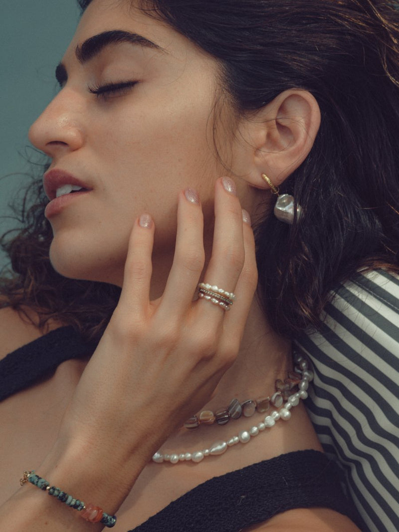 Close-up of a woman wearing earrings, rings, and a necklace with a blurred background
