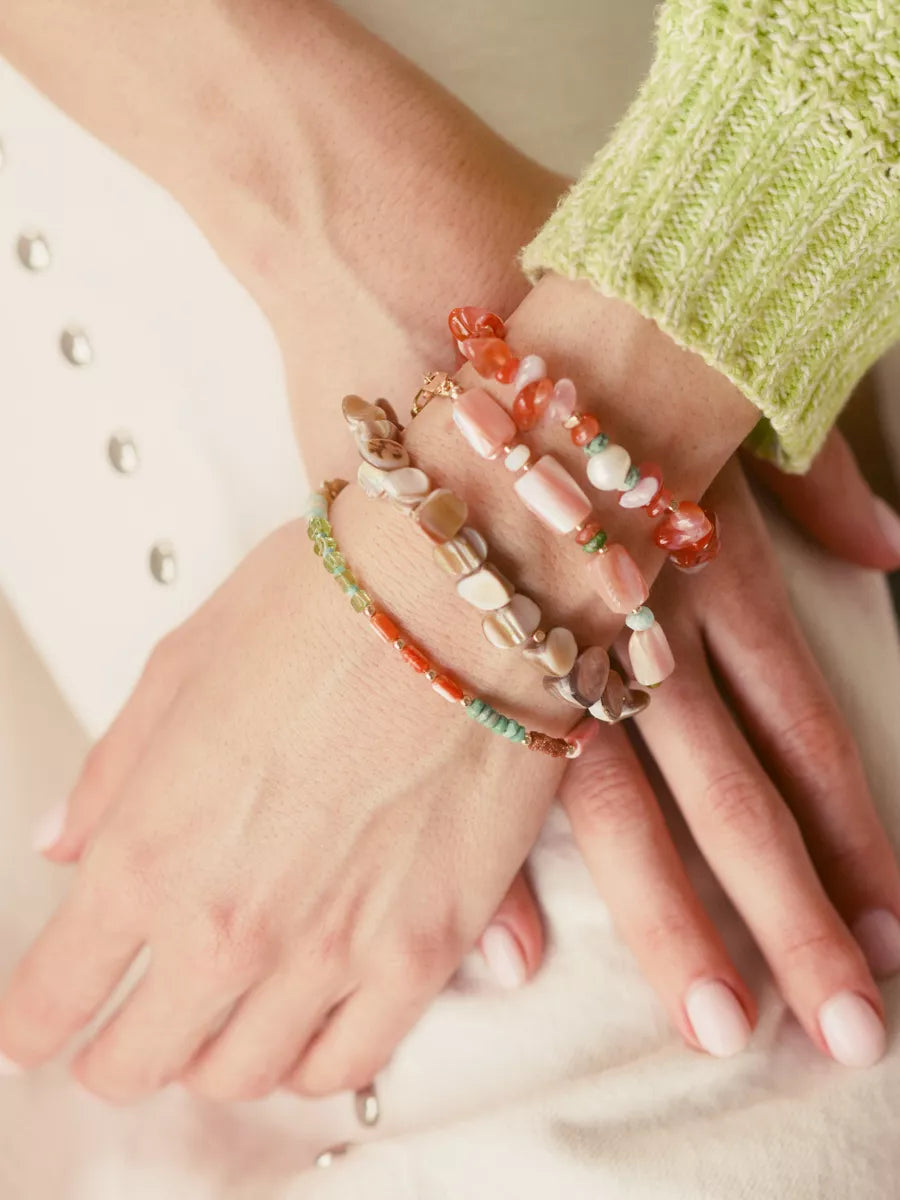 Close-up of hands wearing colorful beaded bracelets on a neutral background
