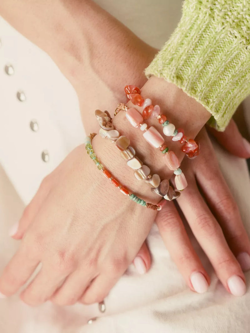Close-up of hands wearing colorful beaded bracelets on a neutral background