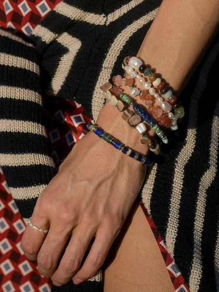 Hand wearing multiple colorful bracelets with a patterned sweater background