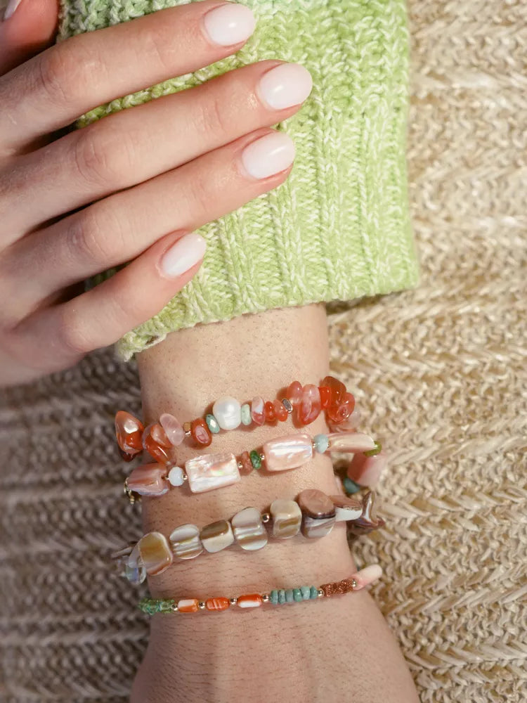 Hand wearing multiple beaded bracelets on a textured surface