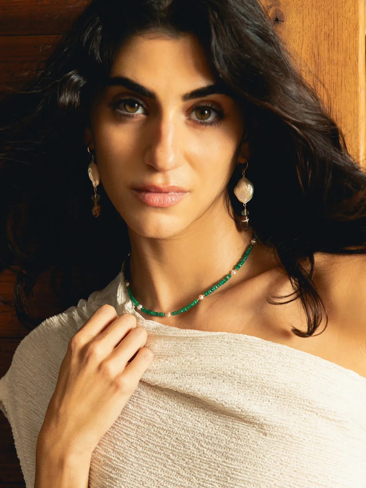 A woman with dark hair models a green beaded necklace and matching drop earrings against a warm wooden background.