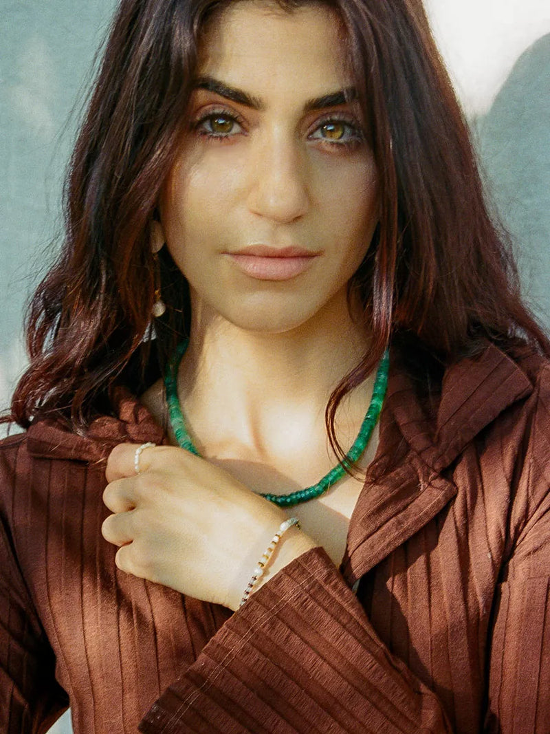 Woman wearing a brown sweater and green necklace against a light background.