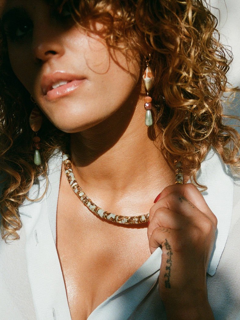 Close up of model wearing shell drop earrings and multicolored necklace.
