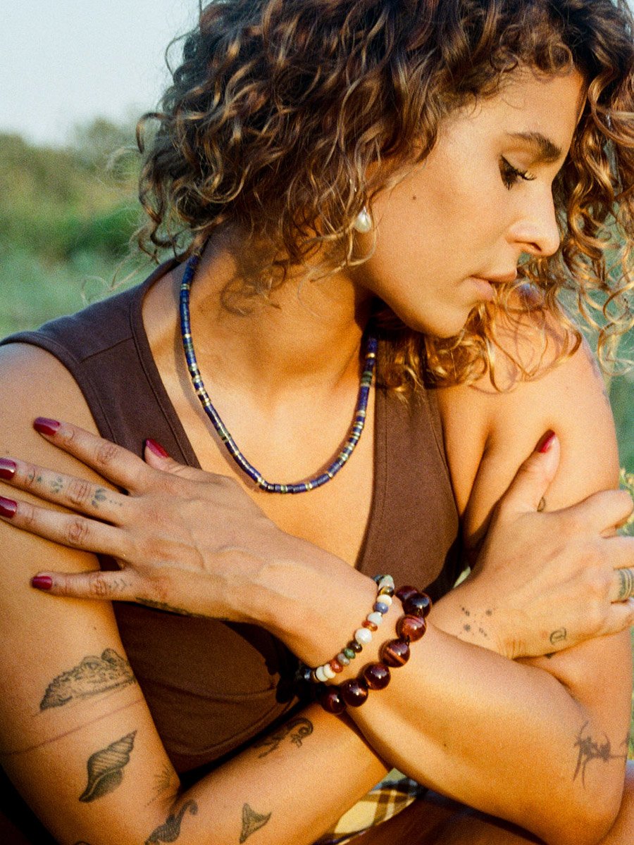 Woman wearing beaded necklace and bracelets in a natural setting.
