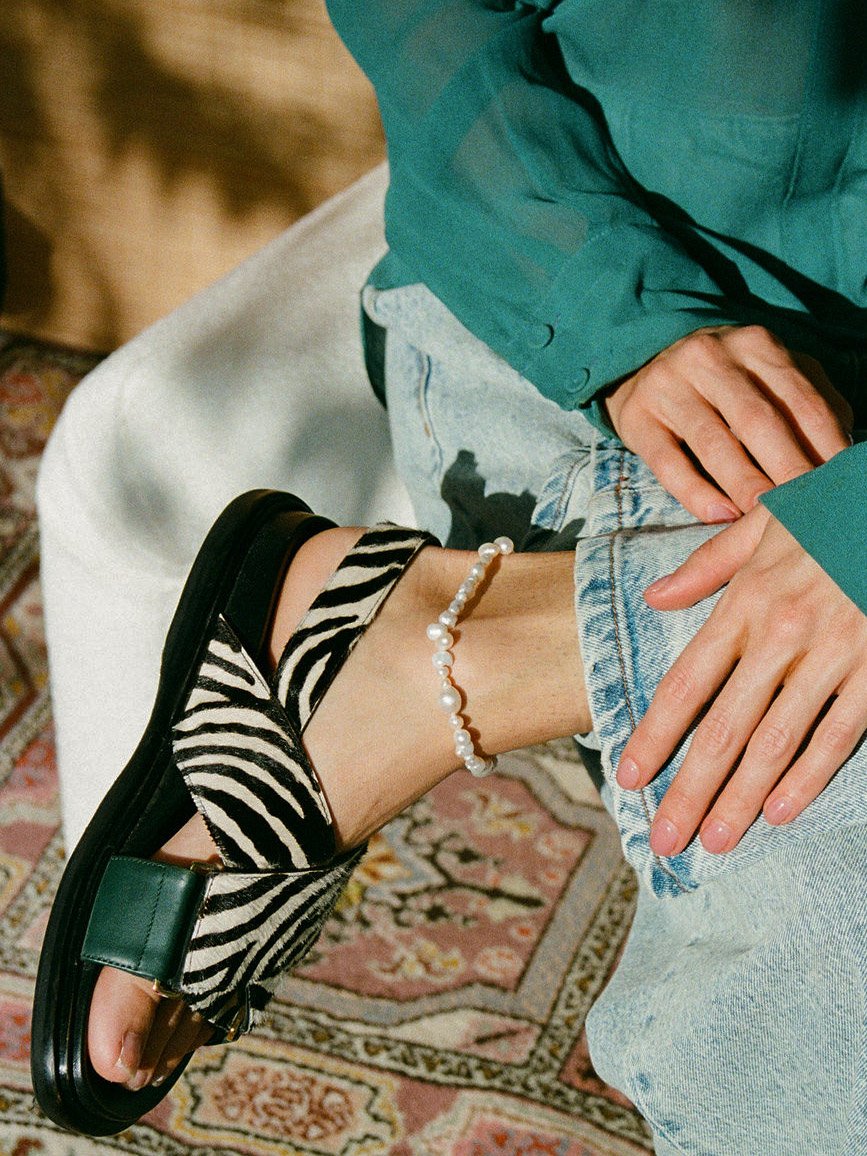 Model wearing zebra print sandals, pearl anklet and turquoise top.