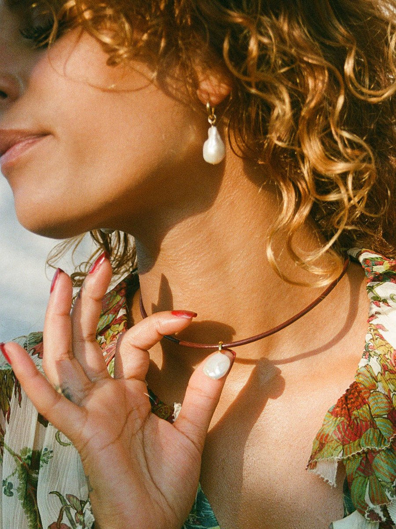 Close up of model wearing a leather necklace with pearl drop pendant.  She is also wearing baroque pearl earrings.