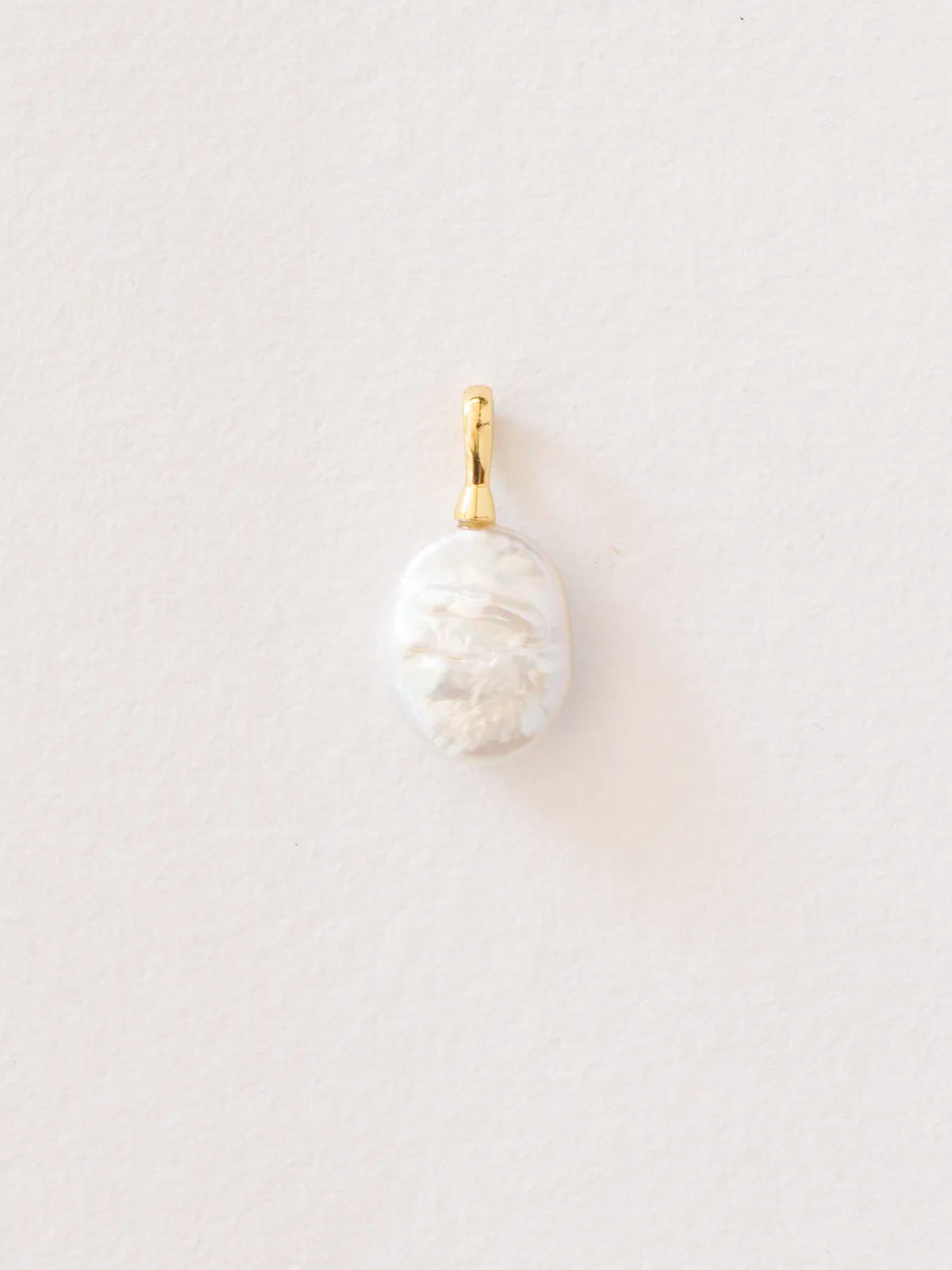 A small oval pendant featuring a carved white mother-of-pearl or pearl with a polished gold bail, shown against a plain, light off-white background.