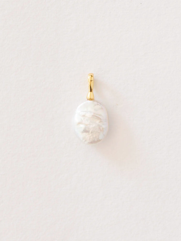 A small oval pendant featuring a carved white mother-of-pearl or pearl with a polished gold bail, shown against a plain, light off-white background.