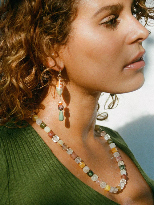 Close-up of a woman wearing a beaded necklace and earrings against a light background