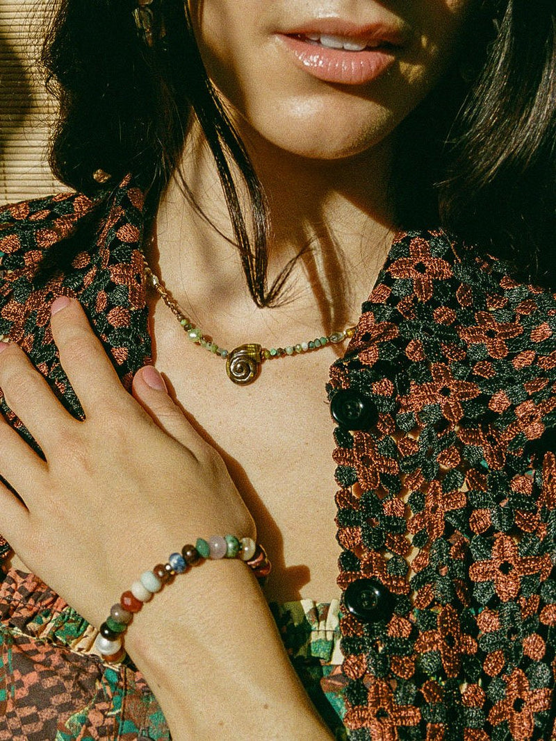 Close up of model wearing multicolored stretch bracelet and tiger's eye snail shell necklace.