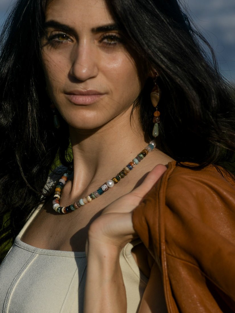 Close up of model wearing a multicolored beaded necklace and holding a leather jacket.