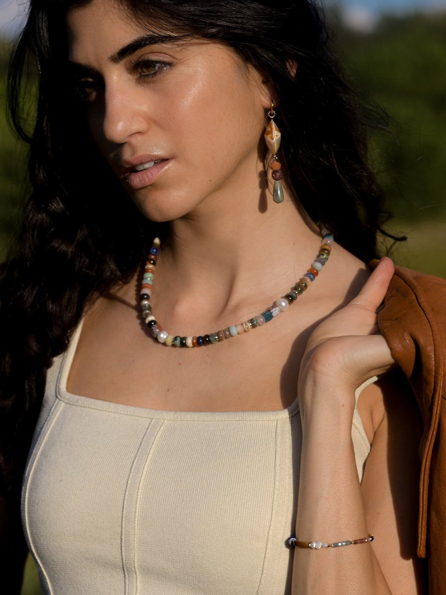 Close up of model wearing a multicolored beaded necklace and holding a leather jacket.