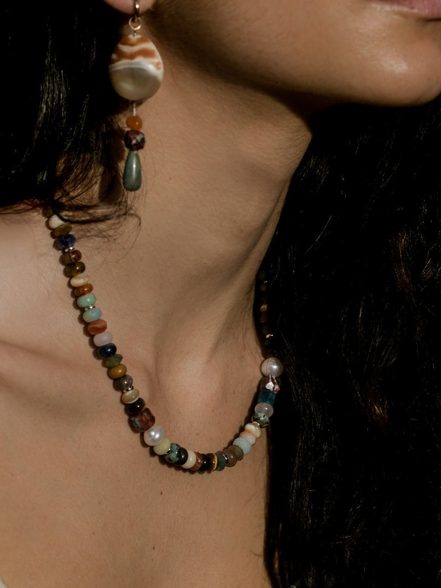 Close up of model wearing a multicolored beaded necklace and shell drop earrings.