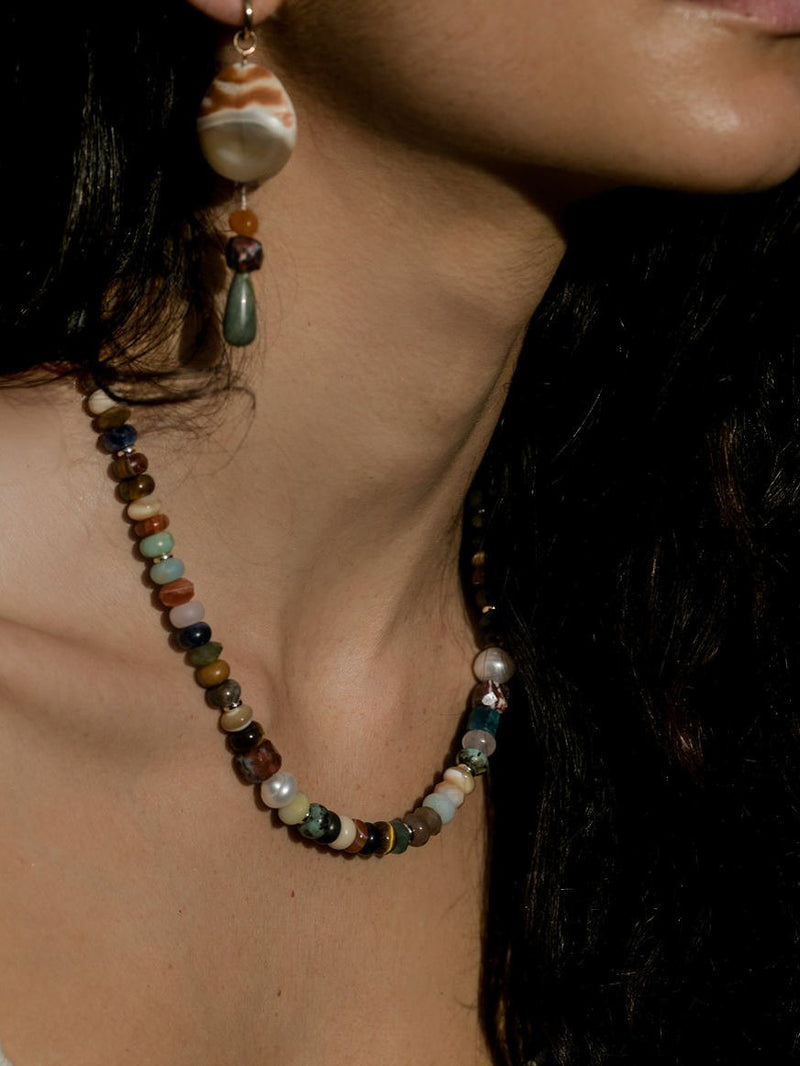 Close up of model wearing a multicolored beaded necklace and shell drop earrings.