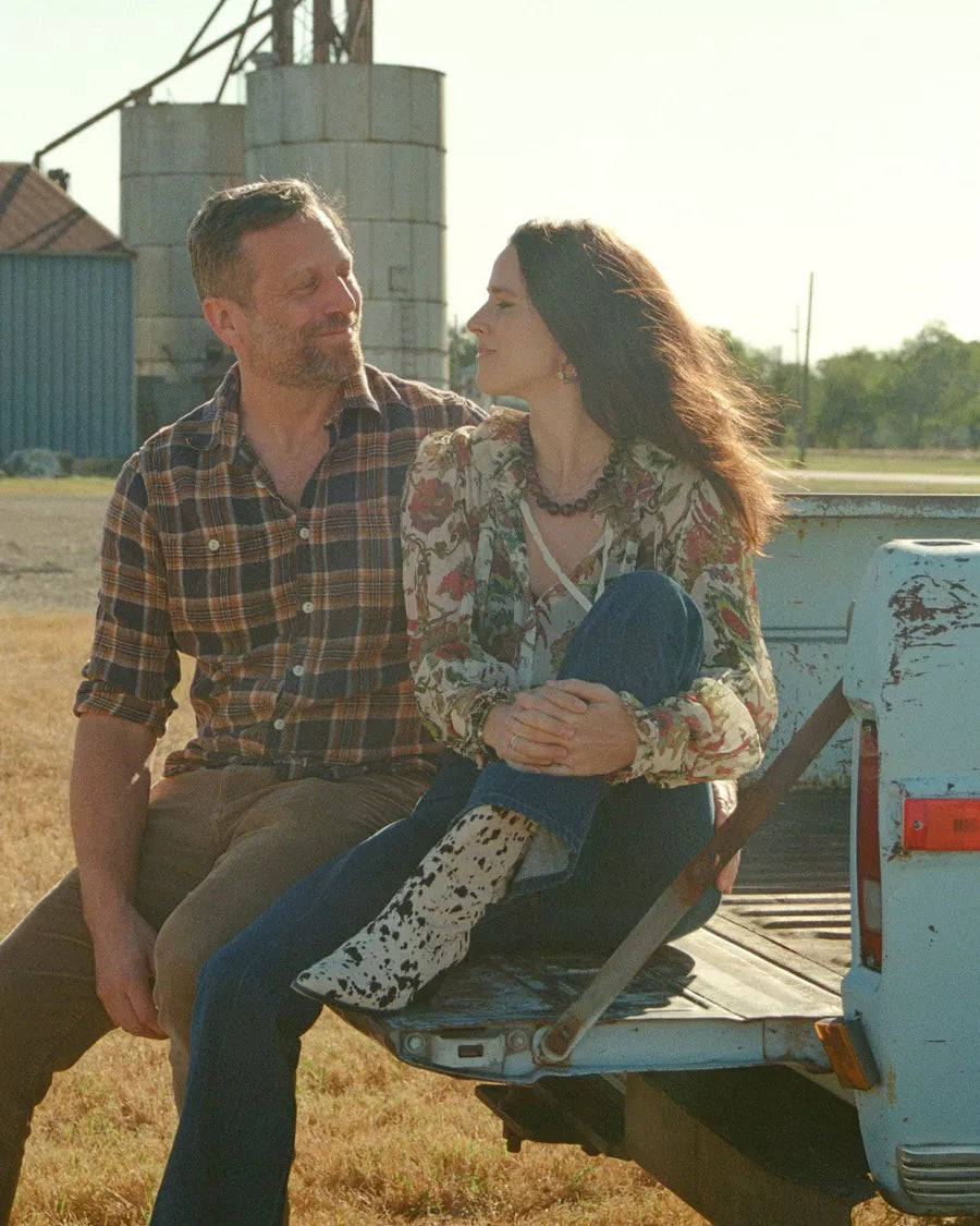 Woman and man sitting on tailgate of a truck in a rural setting.