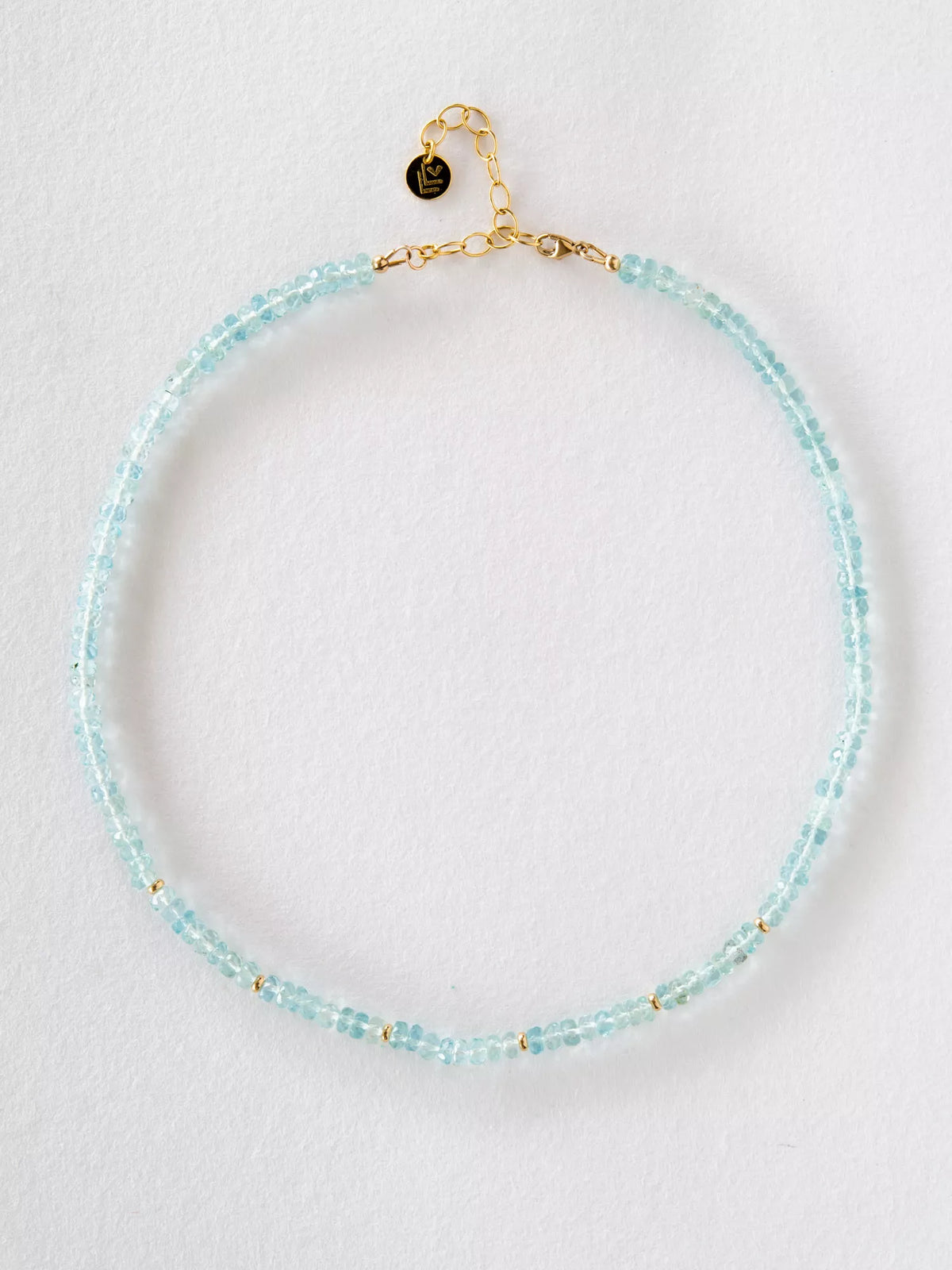 Necklace with aquamarine beads and gold clasp on a light gray background