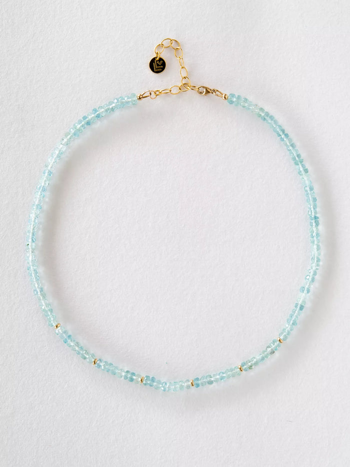 Necklace with aquamarine beads and gold clasp on a light gray background