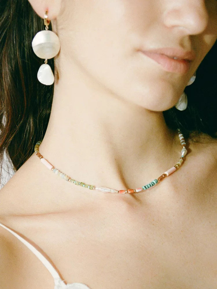 Close-up of a woman wearing pearl earrings and a beaded necklace.