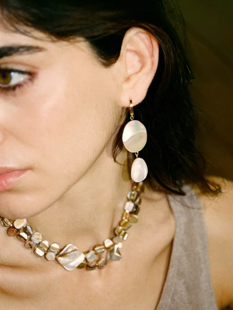 Close-up of a woman wearing a necklace and earrings with a neutral background