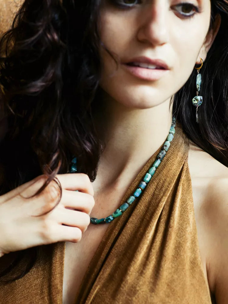Woman wearing a green beaded necklace and earrings, with a blurred background