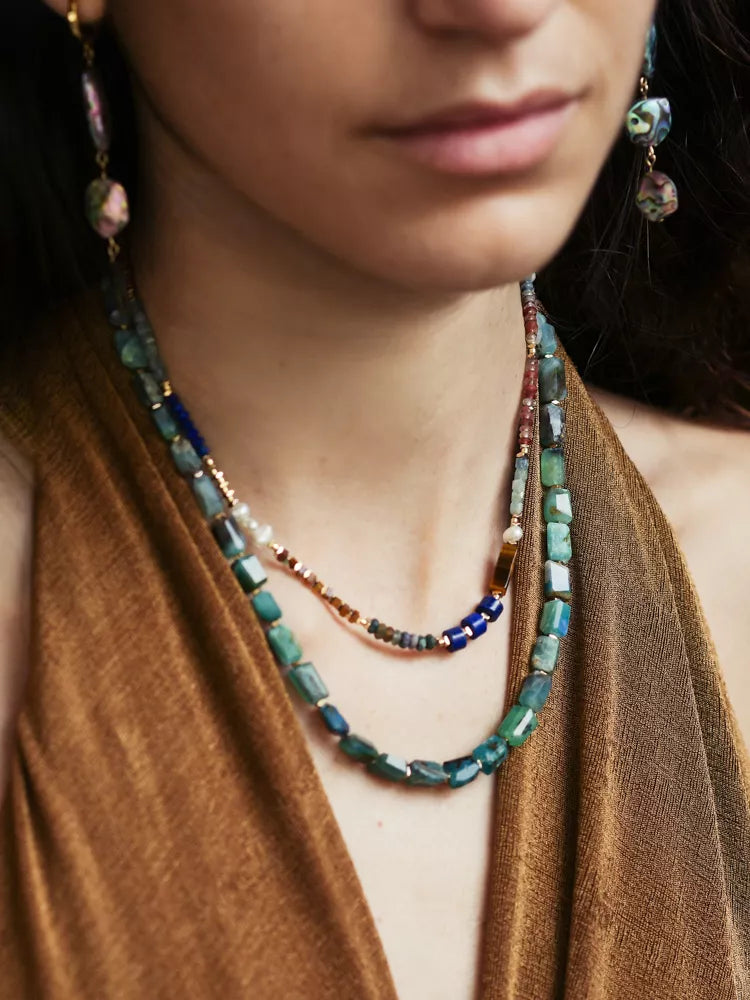 Close-up of a person wearing a beaded necklace and earrings with a brown top.